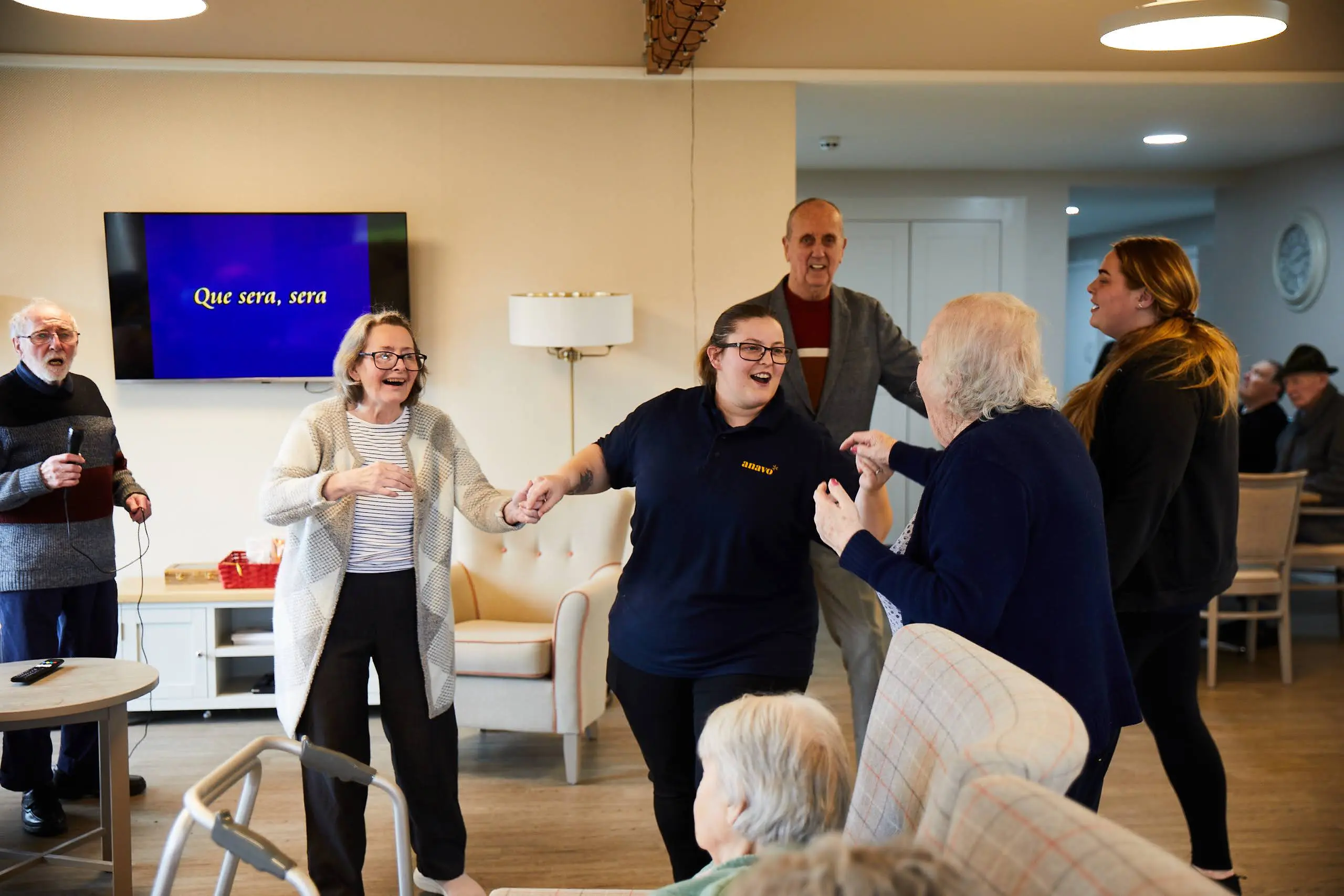 Two elderly ladies and an elderly man dancing with a young with a member of staff.