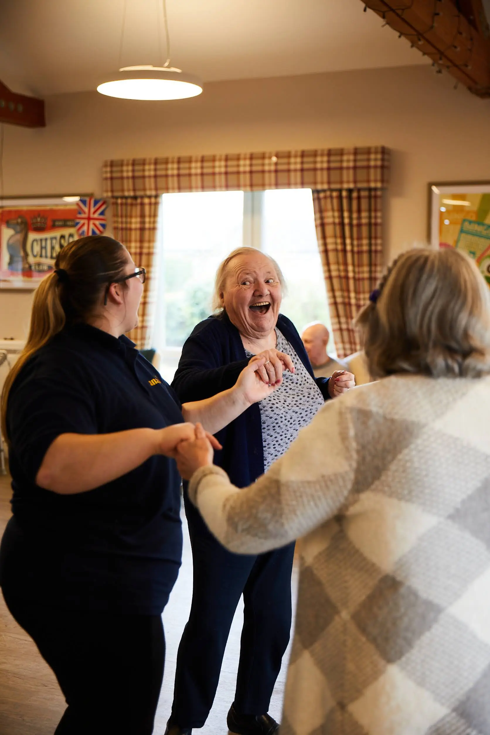 A lady with a happy expression on her face while dancing with another guest and a member of staff in the lounge at Brampton Lodge.