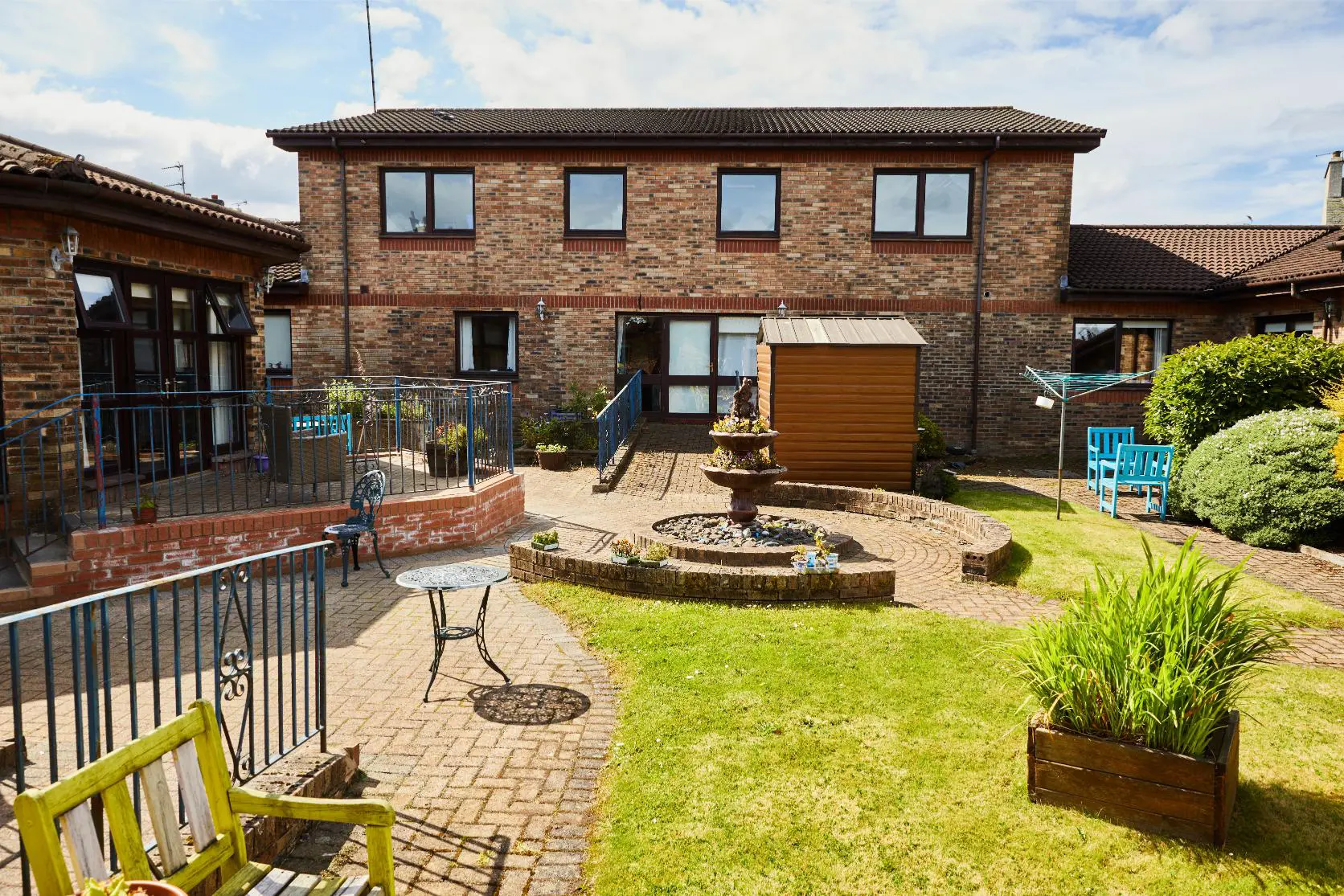 A sunny view of accessible, landscaped garden with the care home building behind it.