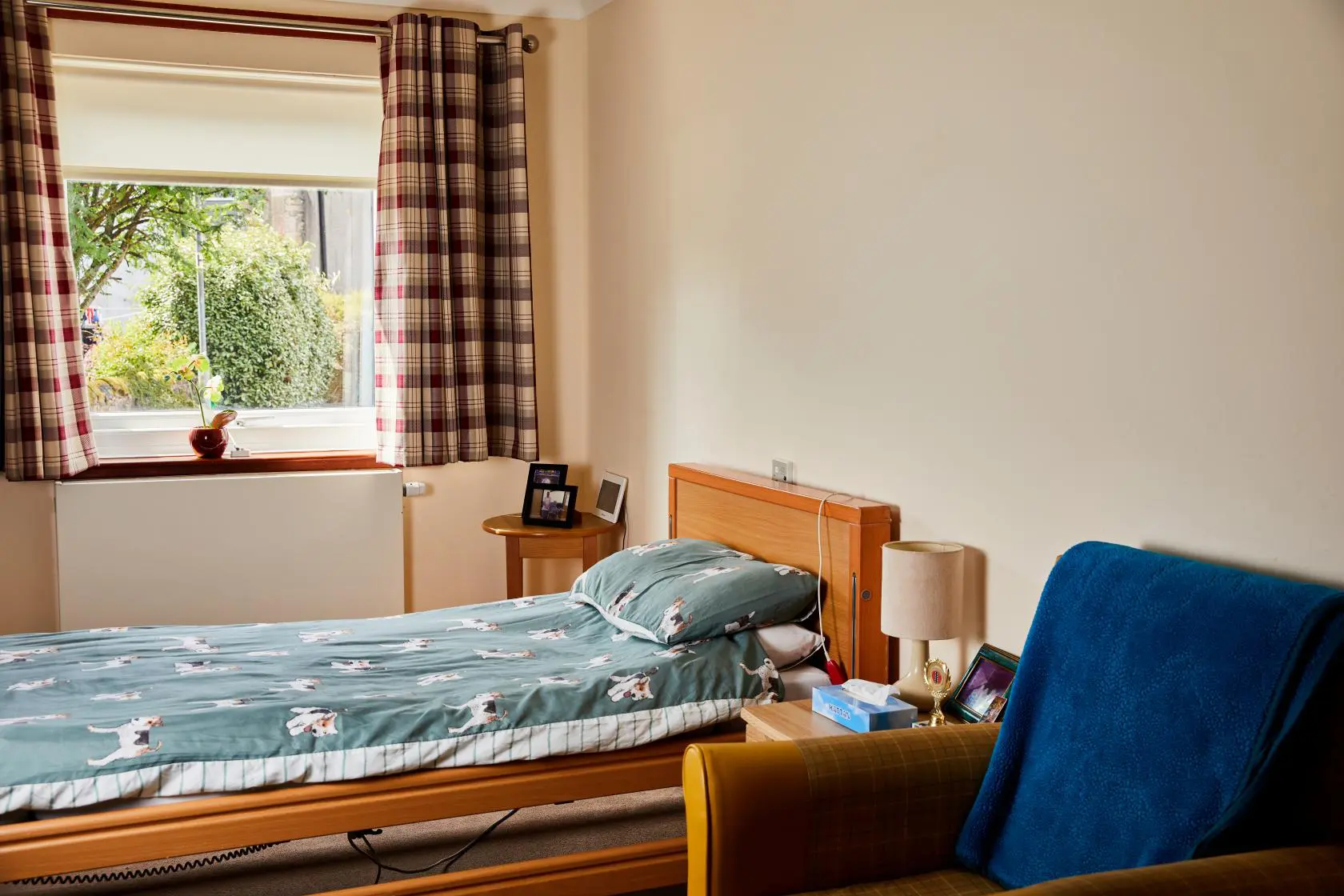 View of a single bed with green and jack russell print duvet in a bedroom at Spiers Care Home.