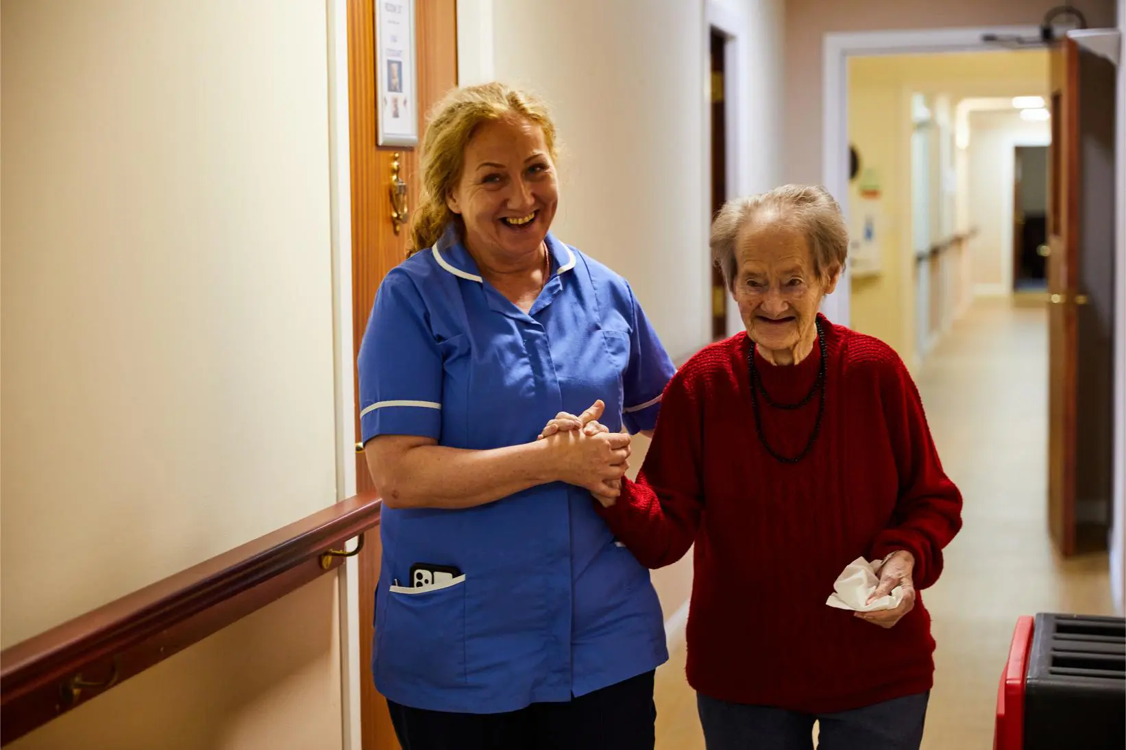 A carer and resident walking down the corridor smiling at Spiers Care Home
