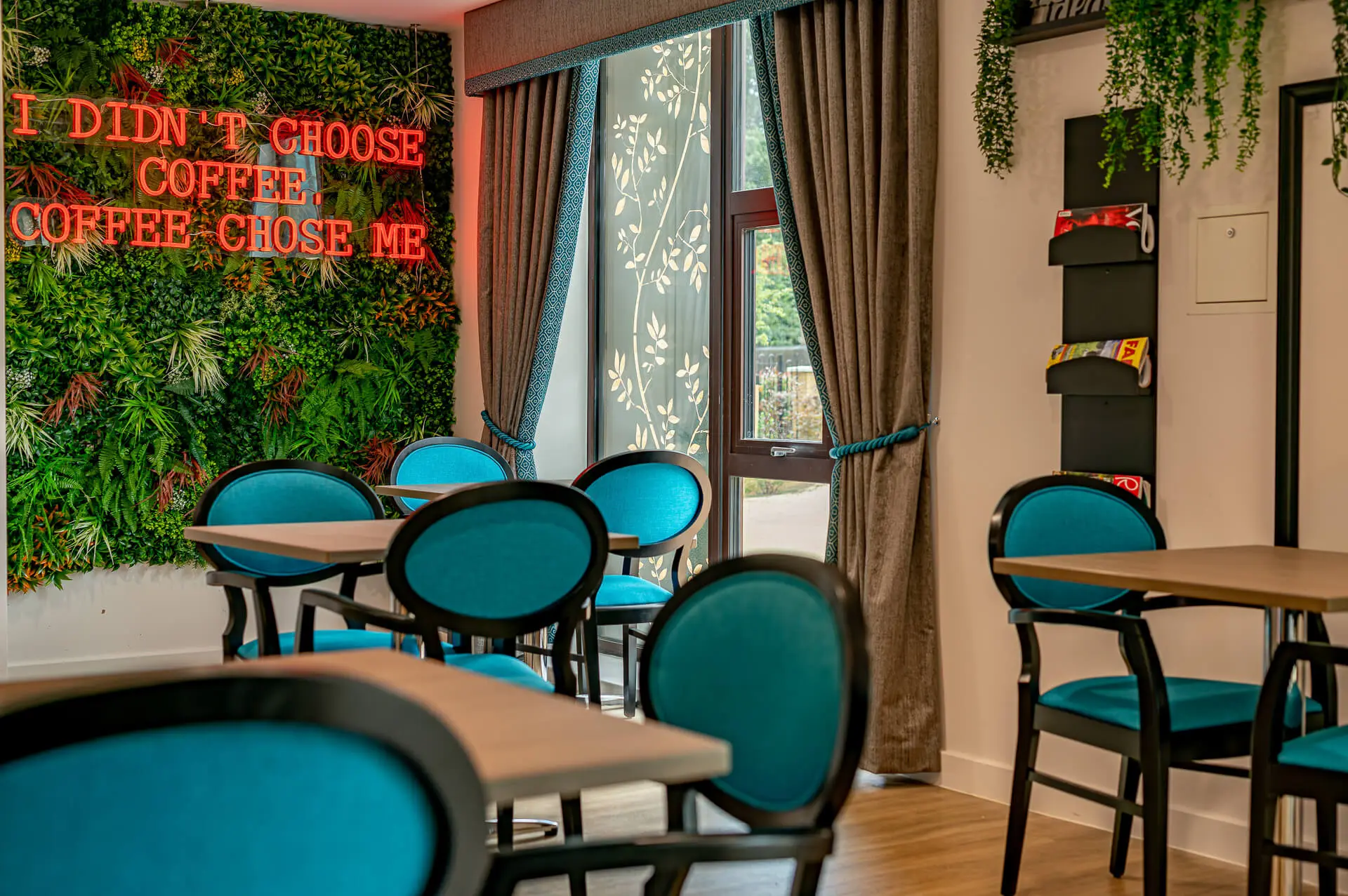 stylish turquoise blue and wood chairs in the vibrant café with neon pink sign in Surbitonian Gardens Care Home cafe.