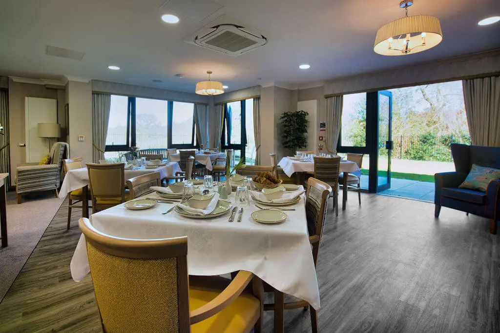 Tables laid with a white cloth and place settings in a large dining room.