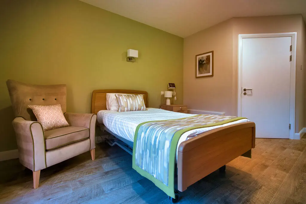 A room with a bed, olive green feature wall and an arm chair.