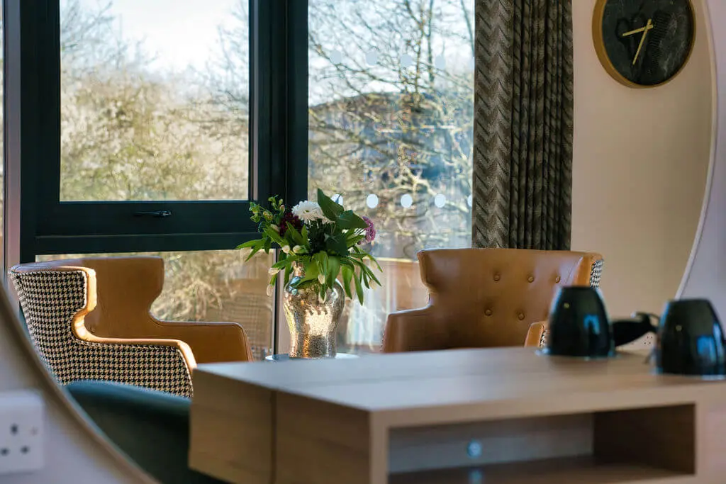 Chars next to a window with a table and vase of flowers.