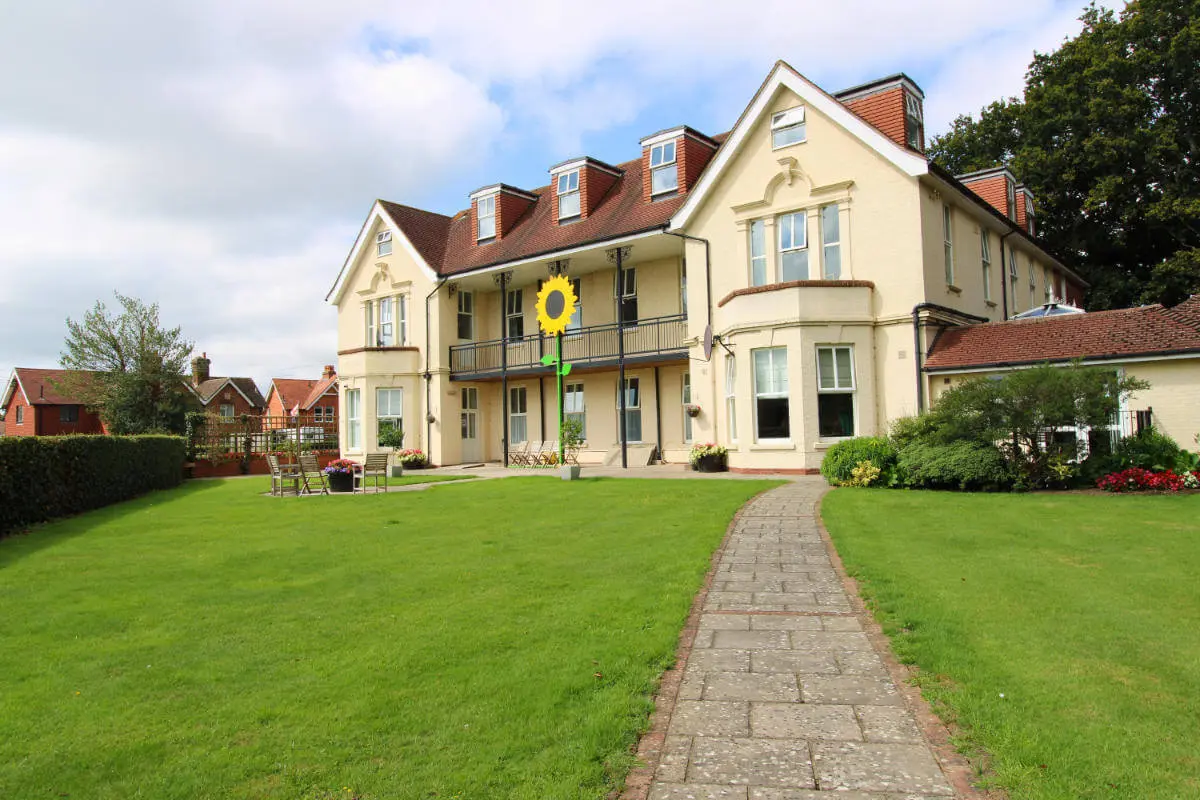 Exterior view of a cream building and lawn with a stone path running up to the building.