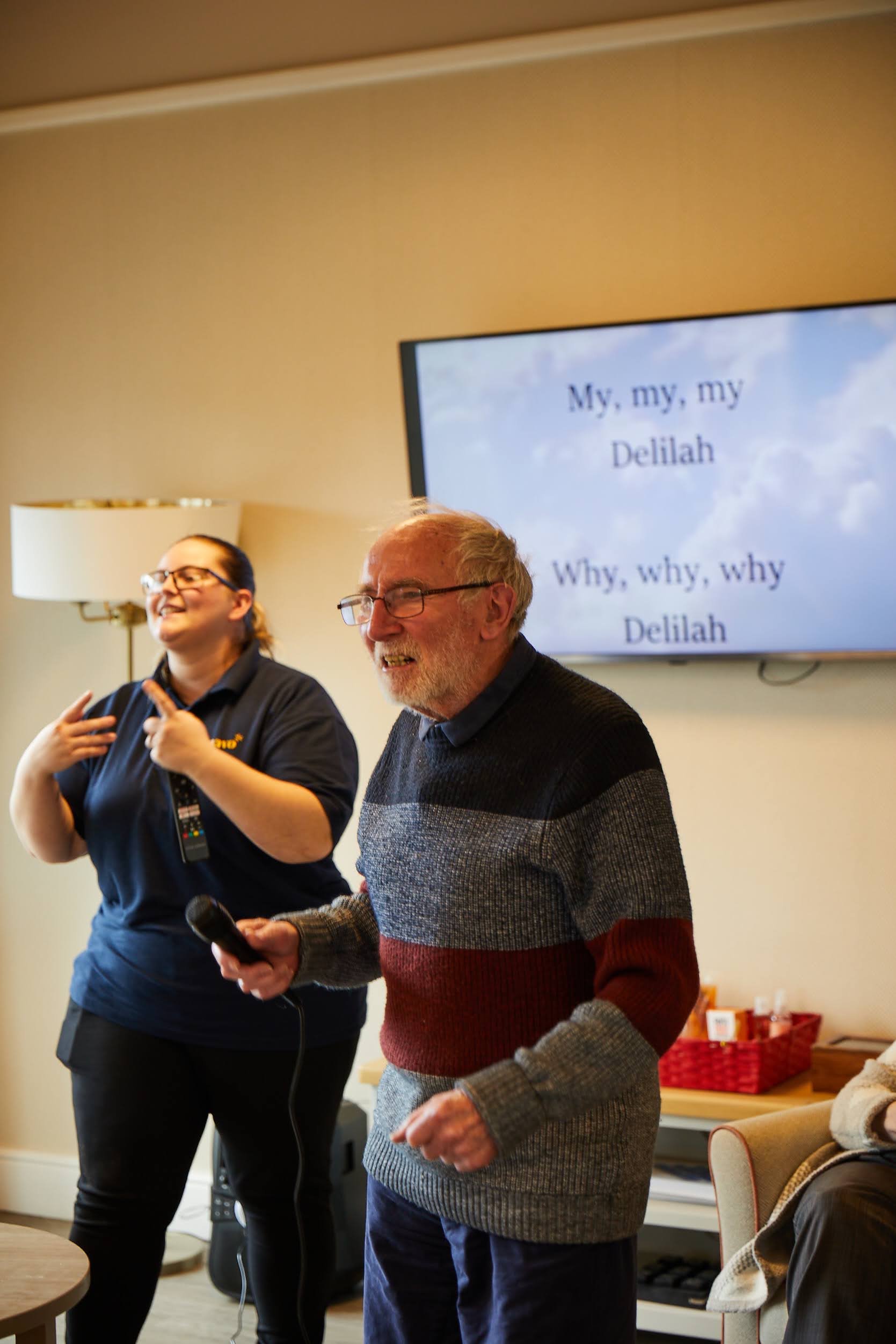 A gentlemen guest holding a mic and singing during a Brampton Lodge Day Centre karaoke activity.