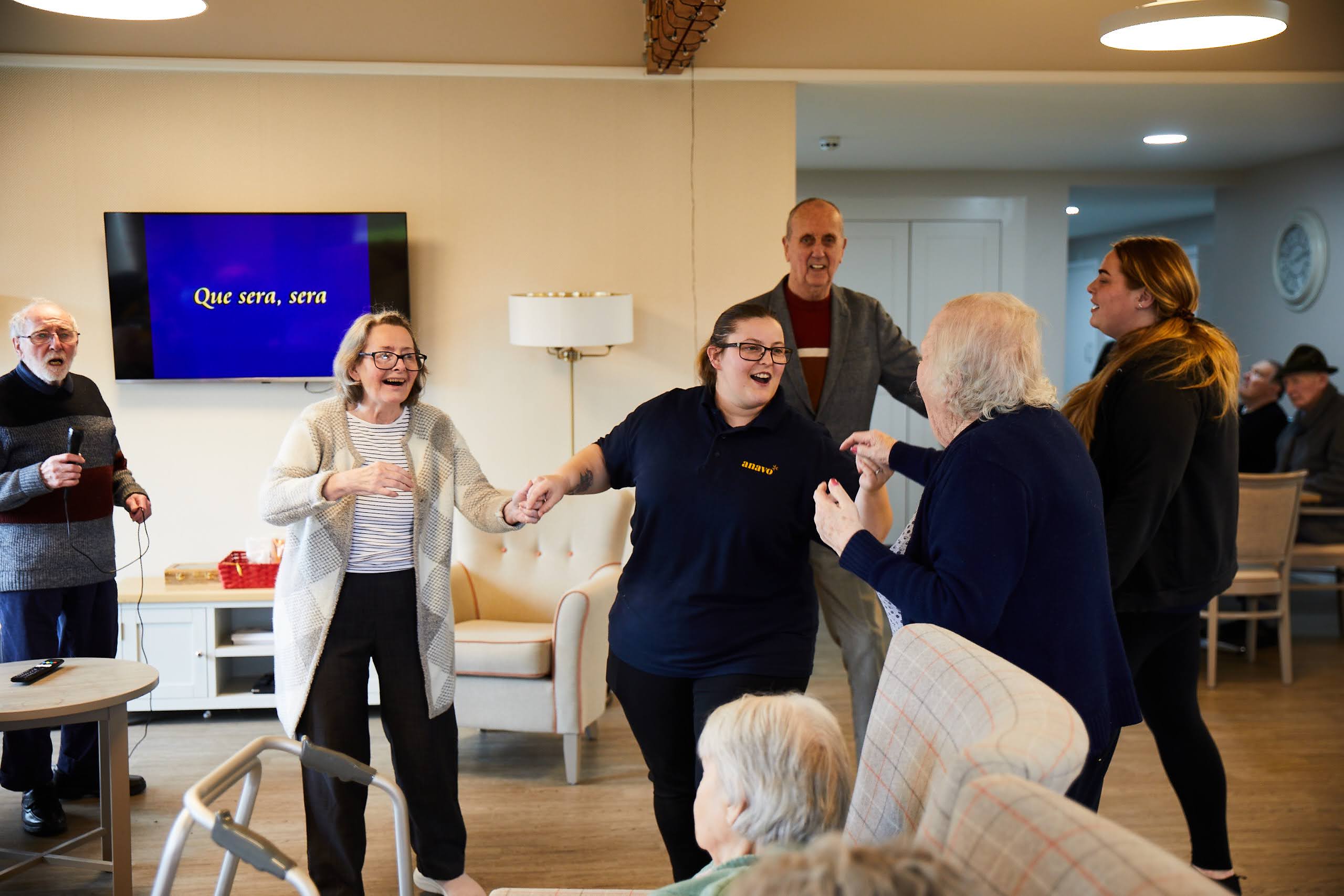 Two elderly ladies and an elderly man dancing with a young with a member of staff.