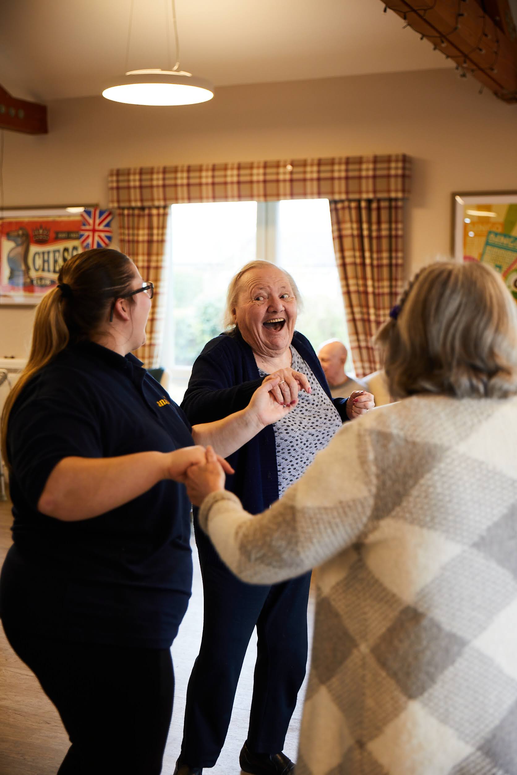 A lady with a happy expression on her face while dancing with another guest and a member of staff in the lounge at Brampton Lodge.