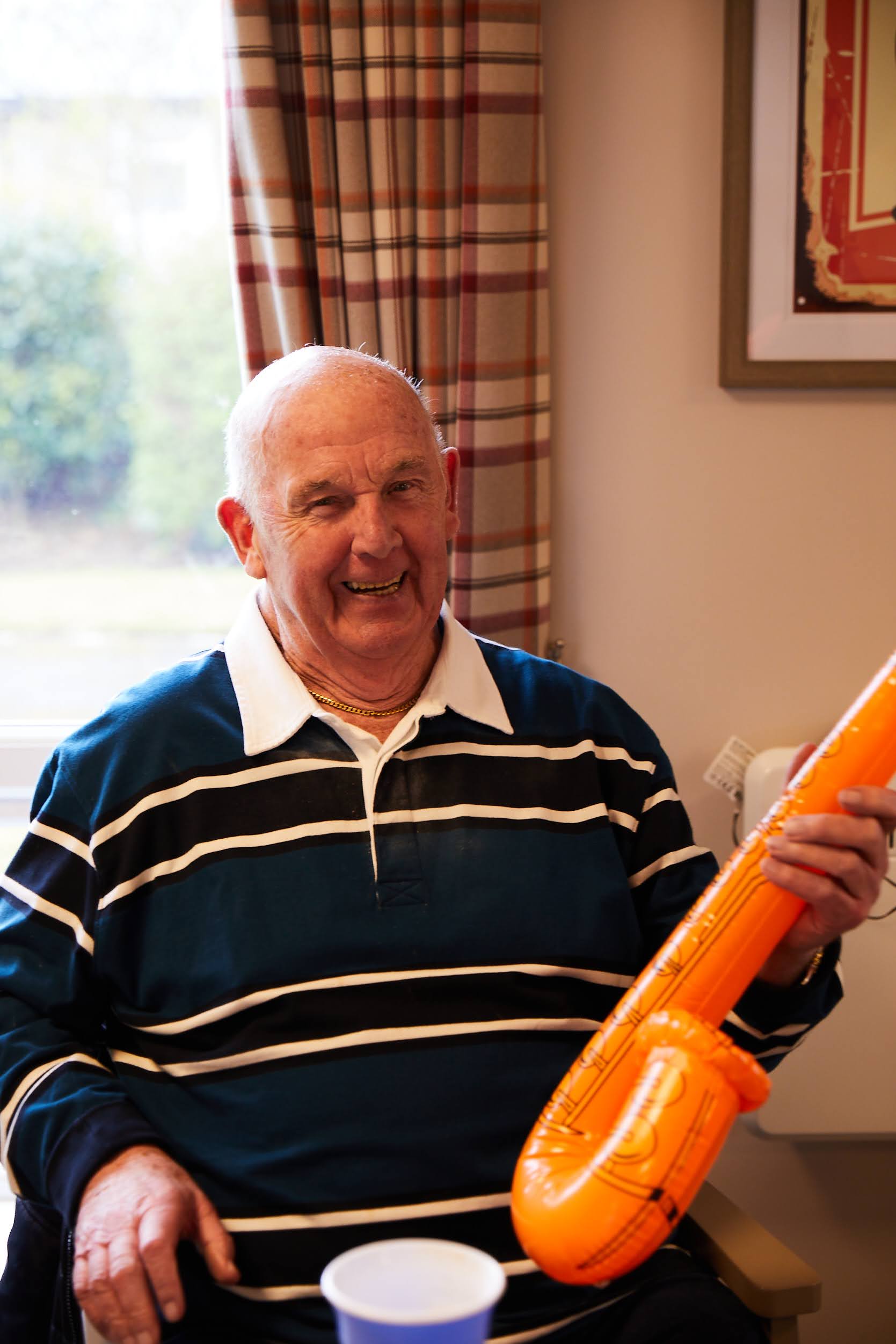 A male guest sat down holding a with a blow-up saxophone at Brampton Day Centre.