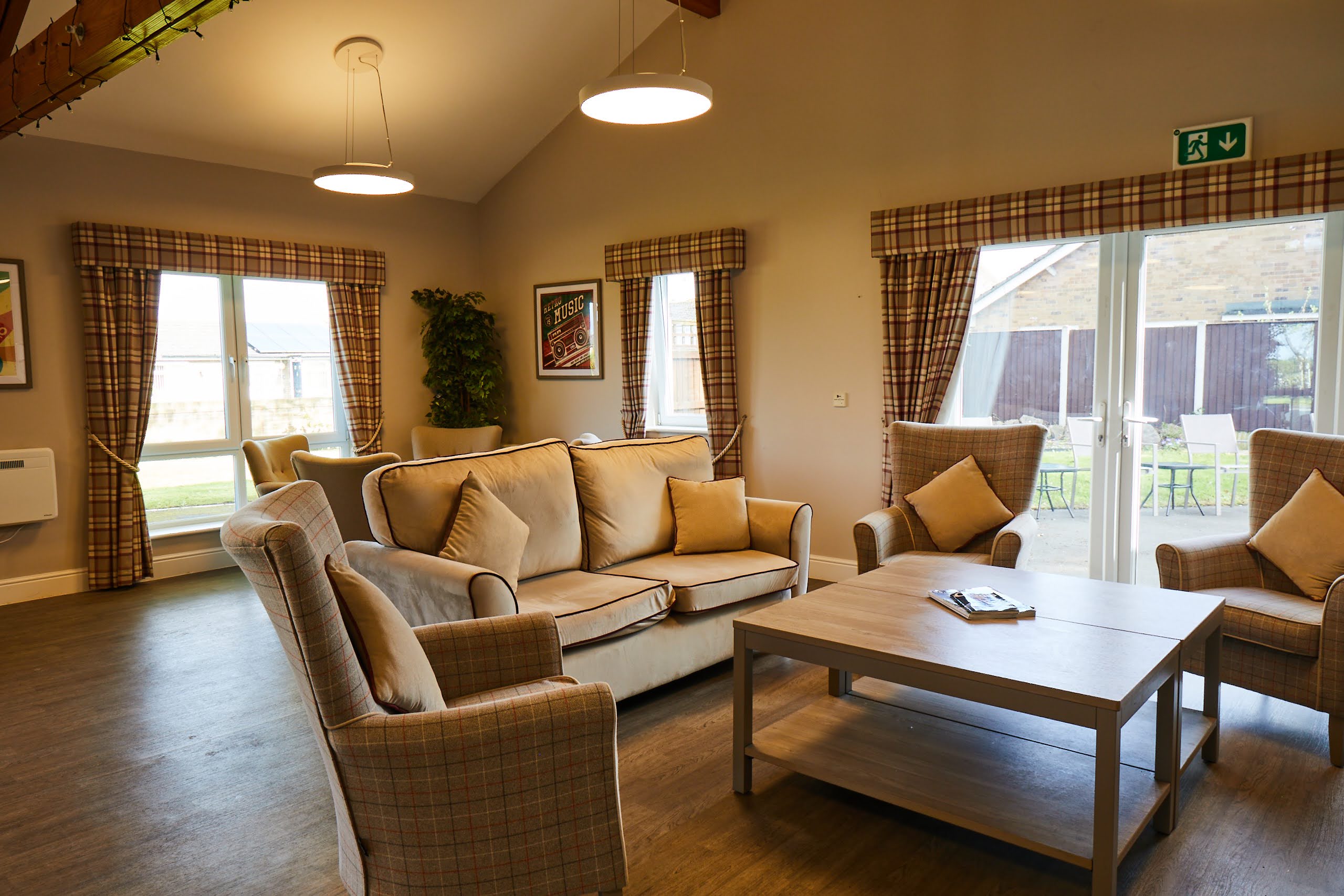 Fawn colour sofa and arm chairs with cushions and a square table in the lounge at Brampton Lodge Day Centre.