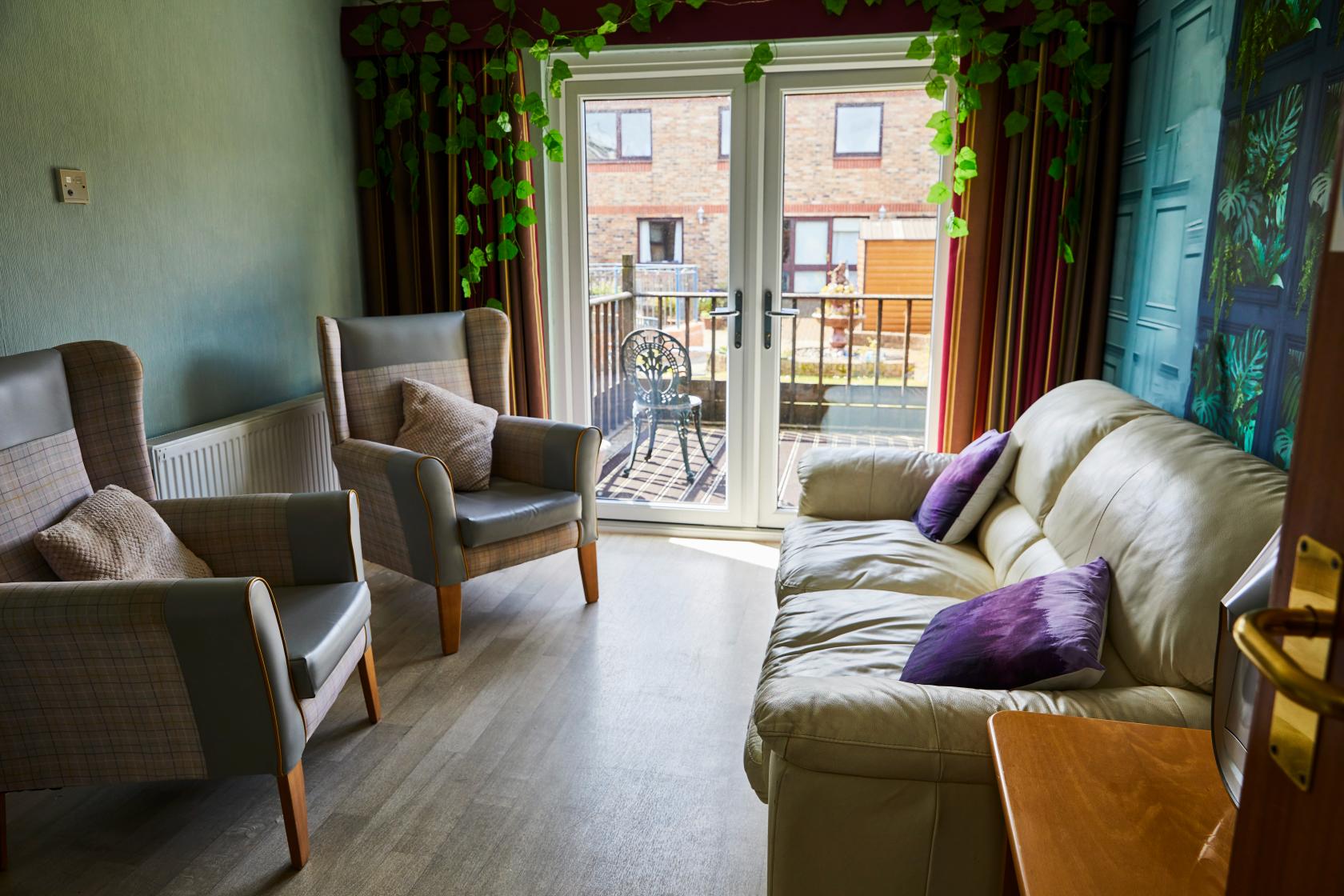 Comfortable sofa and arm chairs with purple throw cushions in a lounge area at Spiers Care Home