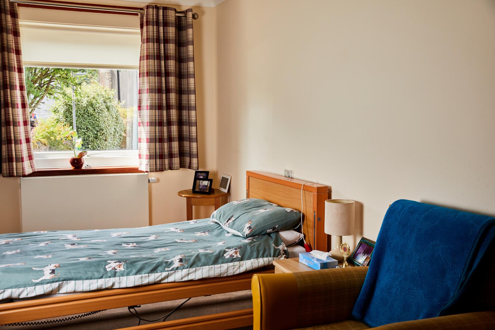 View of a single bed with green and jack russell print duvet in a bedroom at Spiers Care Home.