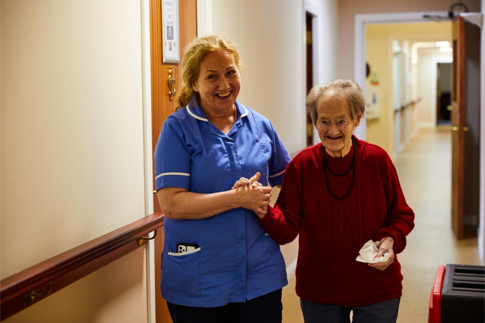 A carer and resident walking down the corridor smiling at Spiers Care Home