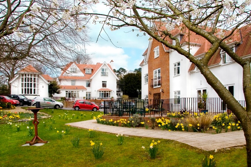 View of large white building with grass and yellow daffodils outside