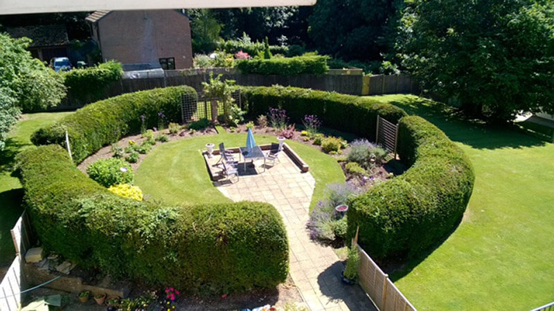 A circular garden surrounded by a trimmed hedge with a path leading to a central patio