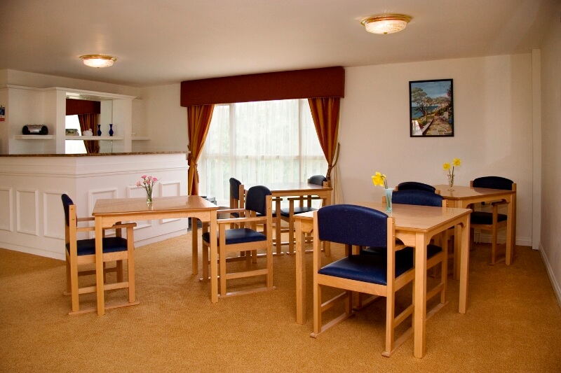 Blue backed wooden chairs and tables in the dining room at Marlborough House Care Home