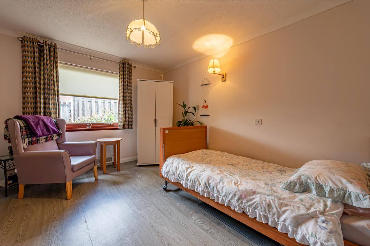 View of the bed, arm chair and wardrobe in a bedroom at Spiers Care Home.