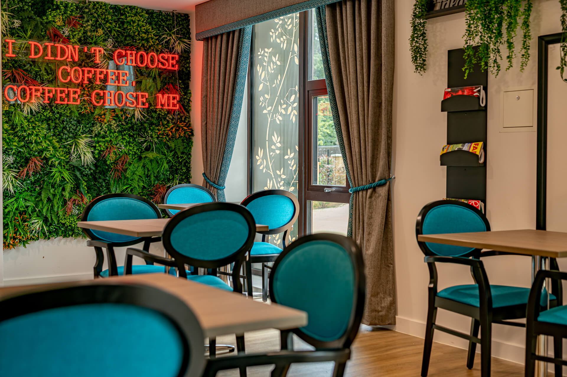 stylish turquoise blue and wood chairs in the vibrant café with neon pink sign in Surbitonian Gardens Care Home cafe.