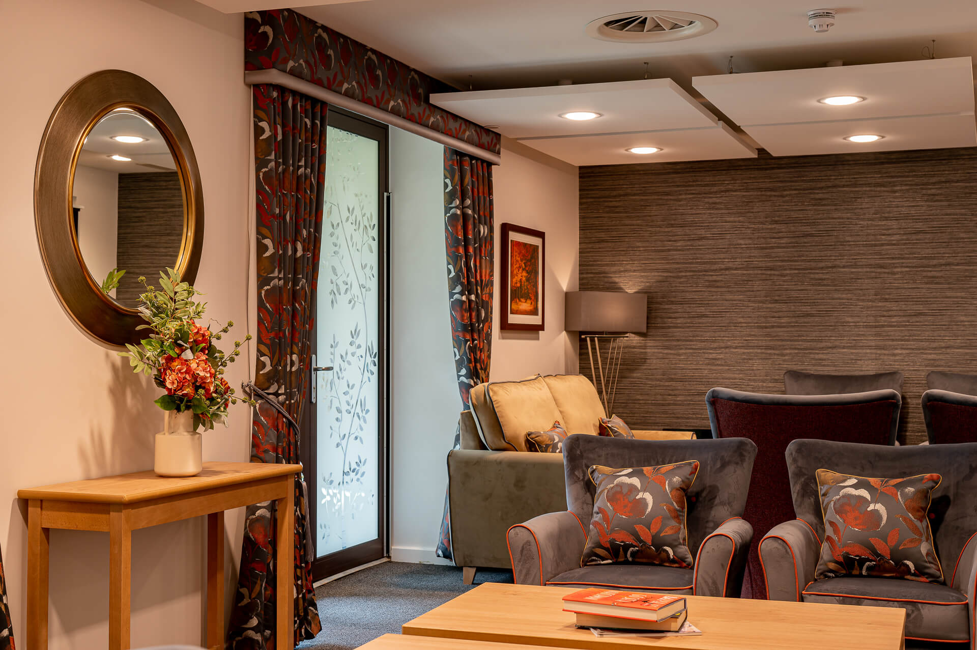 Grey sofas with a red trim and cushions in a lounge at Surbitonian Gardens Care Home.