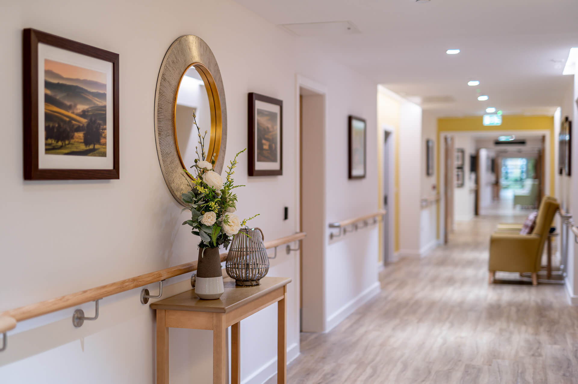 White, spacious hallway with gold trim mirror and flower vase at Surbitonian Gardens Care home.
