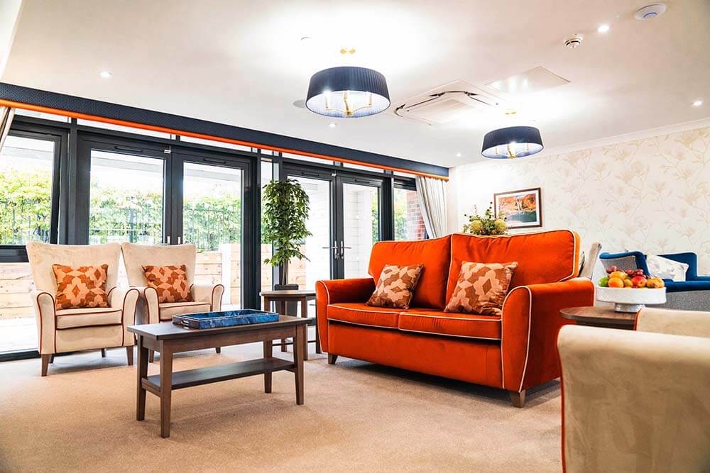 Orange sofa and arm chair with coffee table in front in a lounge at Alexandra Mill Care Home.