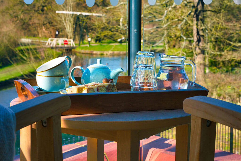 Tray with teapot, cups and cakes in front of a window with a canal-side view.