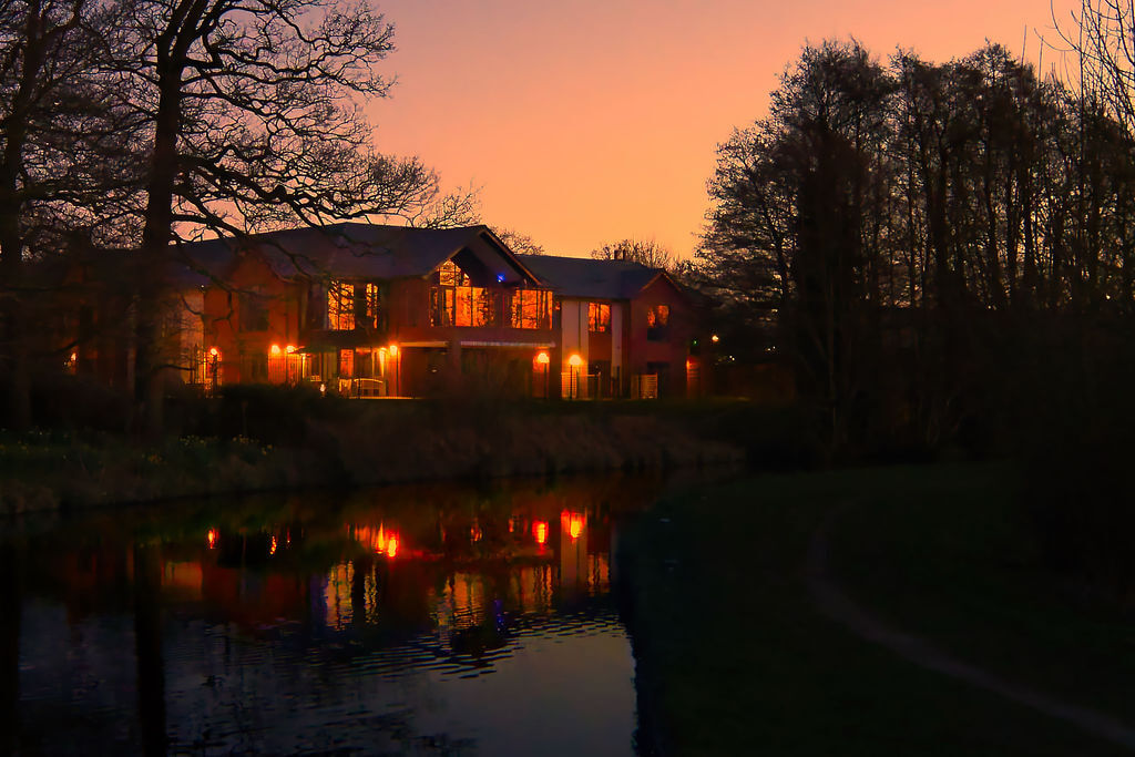 Night time view of building lit up and trees with reflection in water.