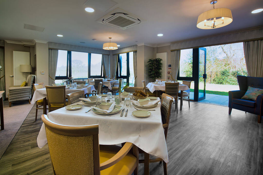 Tables laid with a white cloth and place settings in a large dining room.