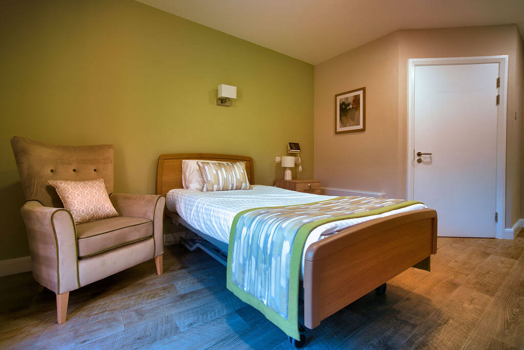 A room with a bed, olive green feature wall and an arm chair.