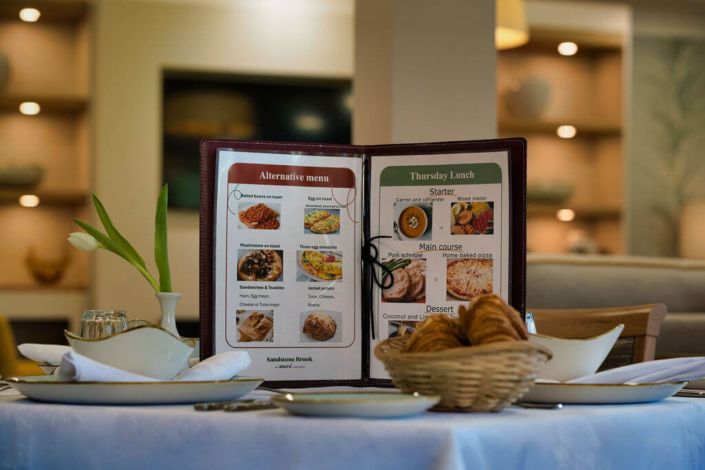 Menu standing on a table laid with place settings for dinner.