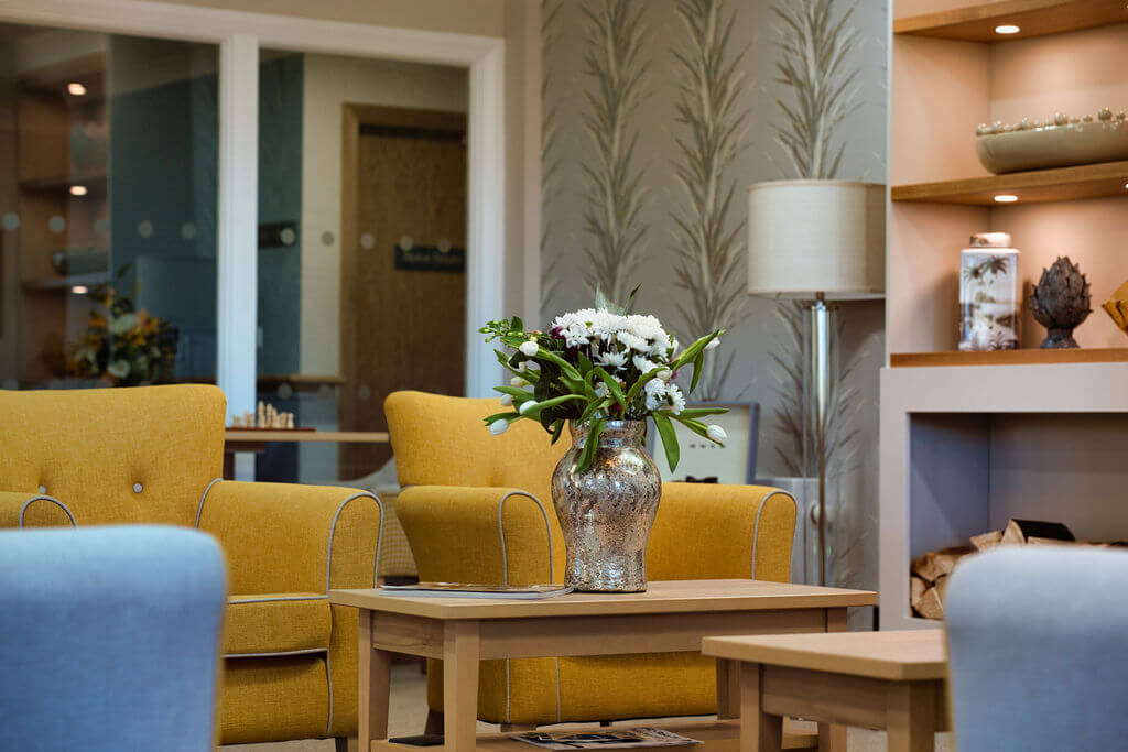 Mustard colour arm chairs next to a table with a vase of flowers on it.