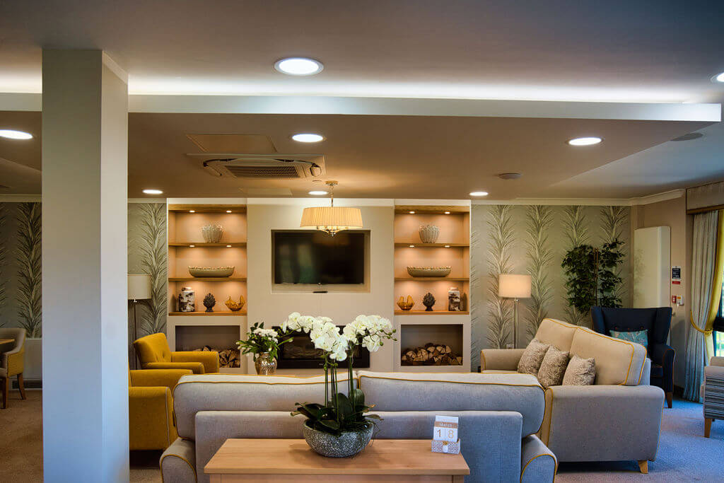 A table with an orchid on it and grey sofas behind it with a TV mounted on the wall.