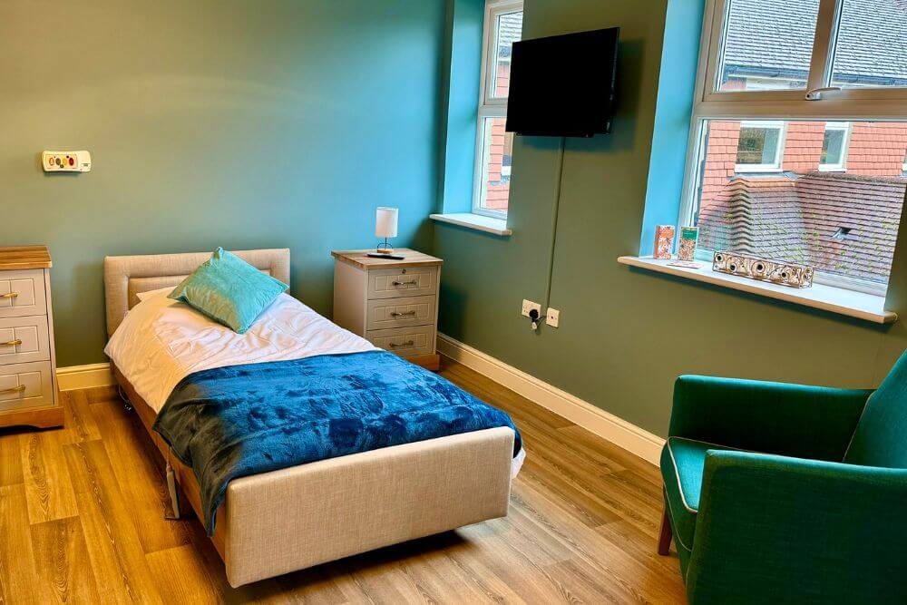 Single bed with teal through cushion and dark blue bed throw on white sheets