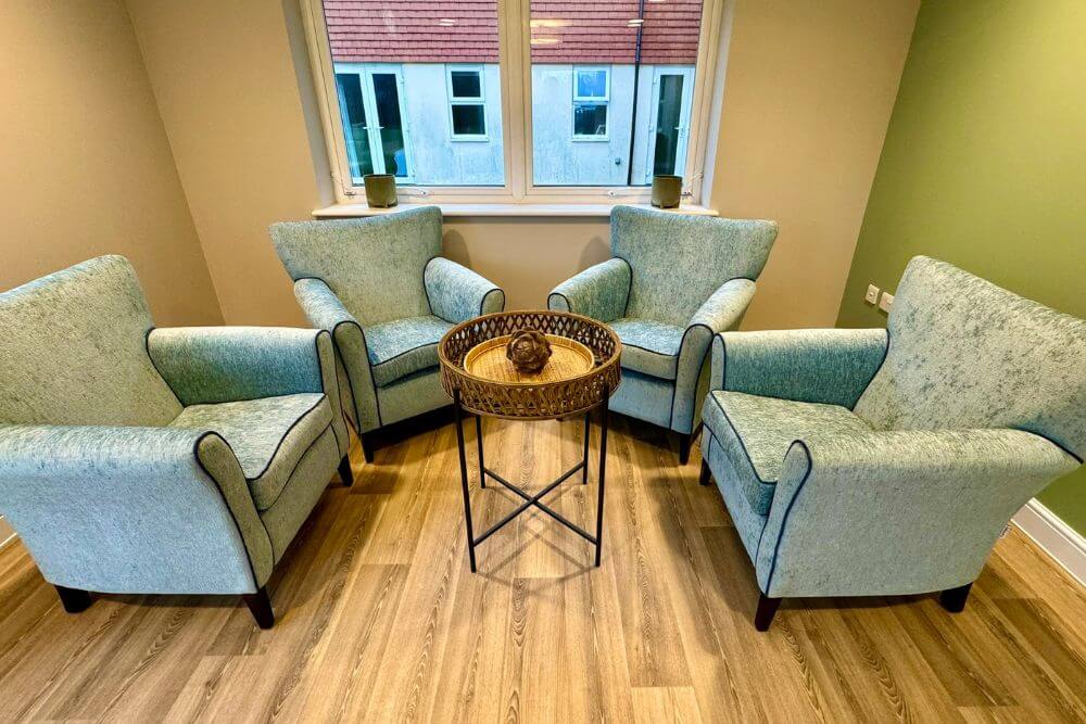 Light blue, fabric arm chairs surrounding a round wooden and metal coffee table.