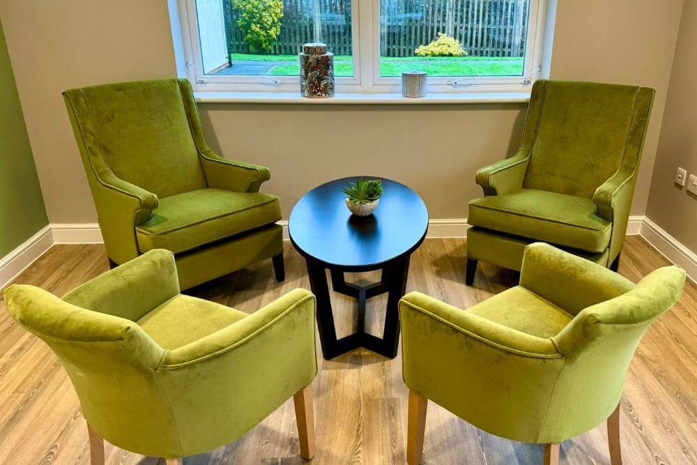 Four, lime green, fabric arm chairs surrounding a wooden, oval coffee table