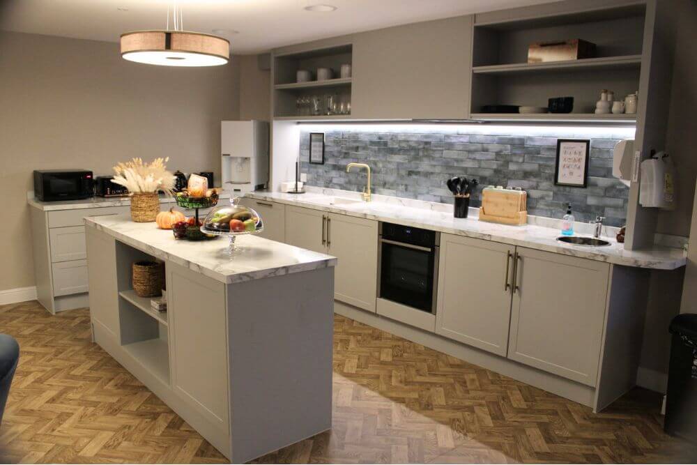 Kitchenette with white cupboards, grey splash back and a white island.