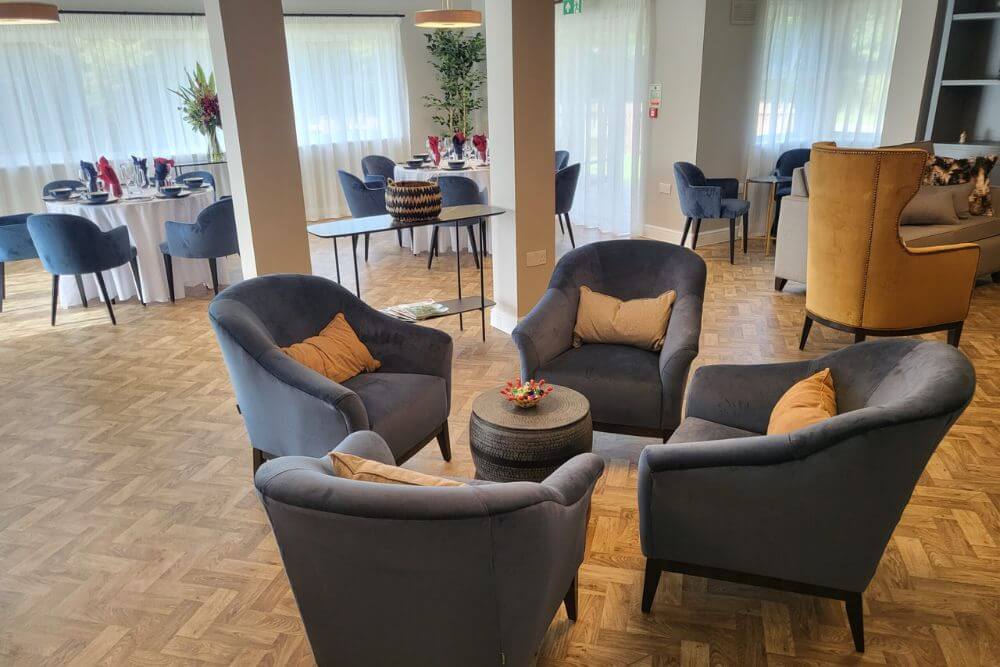 Four grey fabric arm chairs around a coffee table with set dining tables in the background