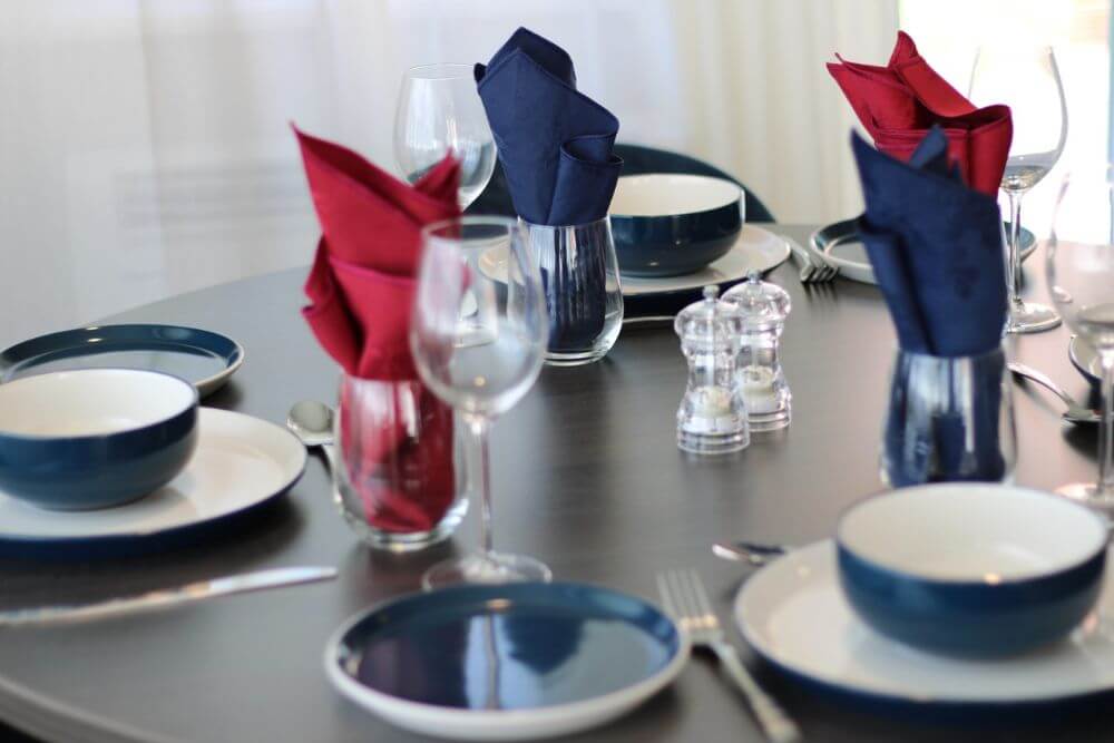 Wine glasses, blue plates and tumblers with red and blue napkins in them on top of a table.