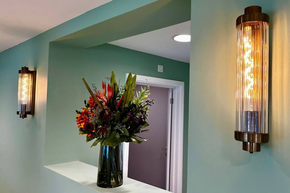 Flowers in a vase on a low wall in a hallway.