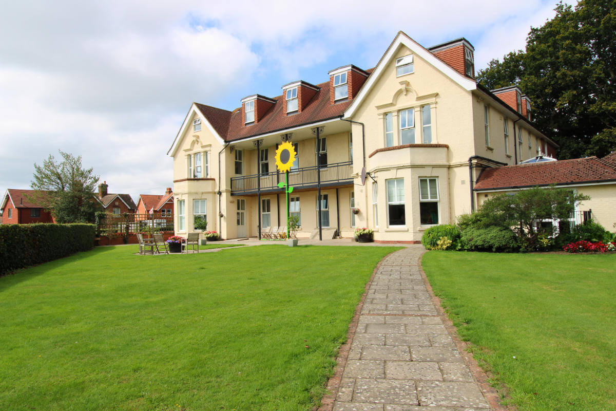 Exterior view of a cream building and lawn with a stone path running up to the building.