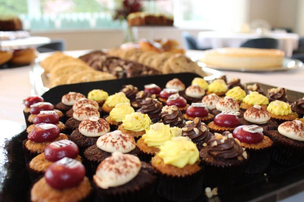 An assotment of homemade cupcakes on a tray with a tray of cookies in the background.