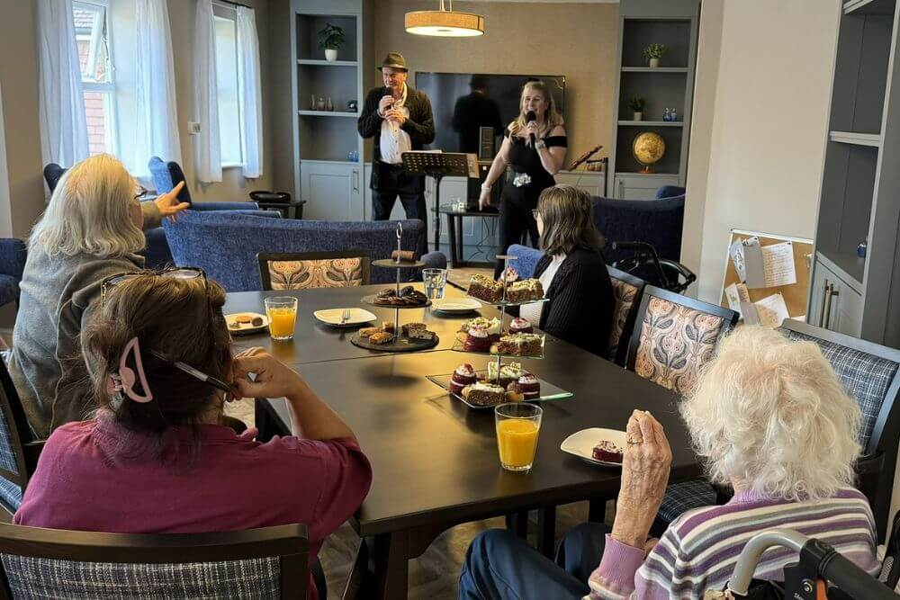 Two people singing to 4 sitting elderly care home residents